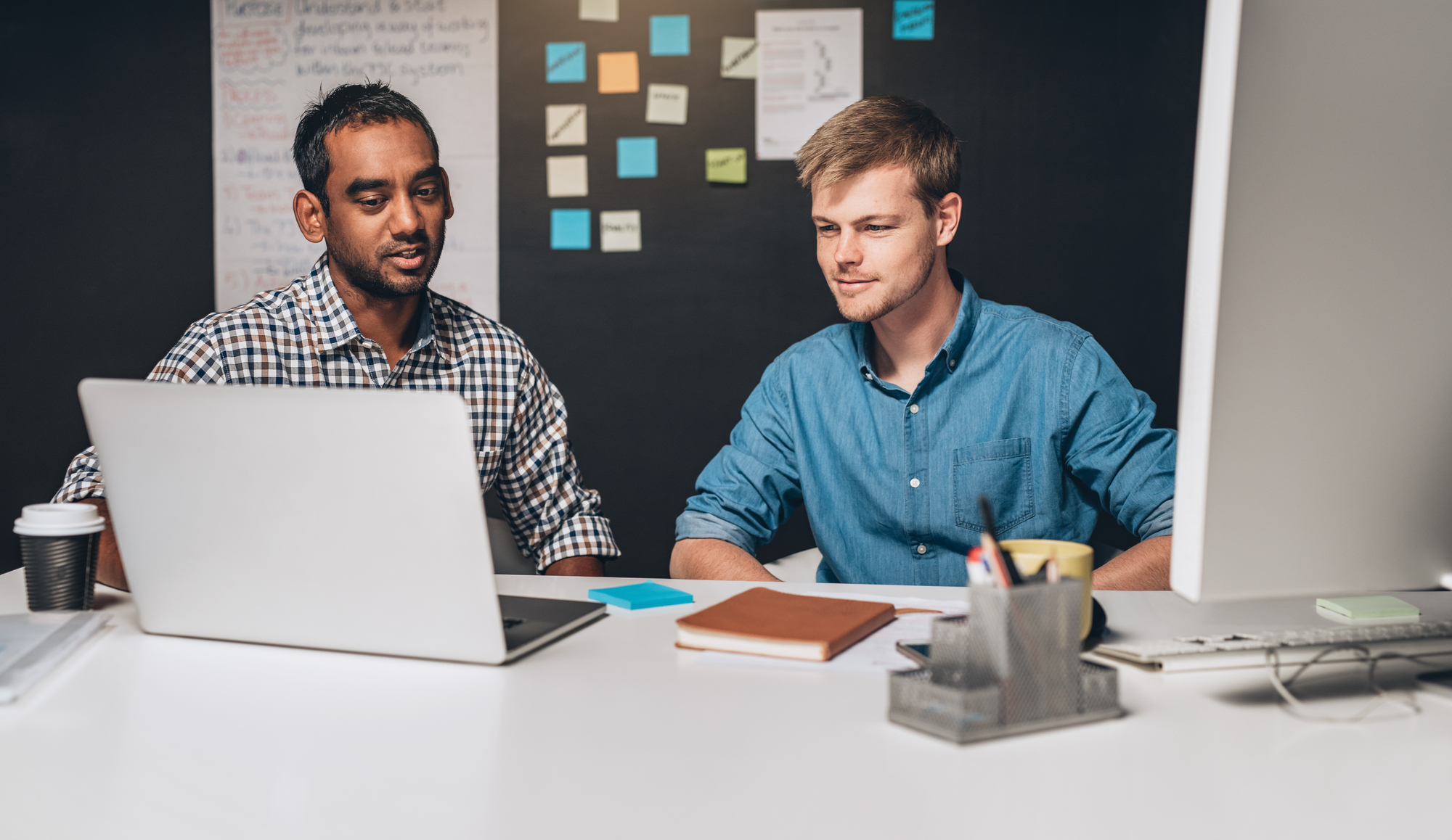 Ein Team von Menschen arbeitet an einem Tisch mit Laptops und Tablets und diskutiert über Daten, die die kollaborative Nutzung von KI in ERP/CRM-Systemen darstellen.